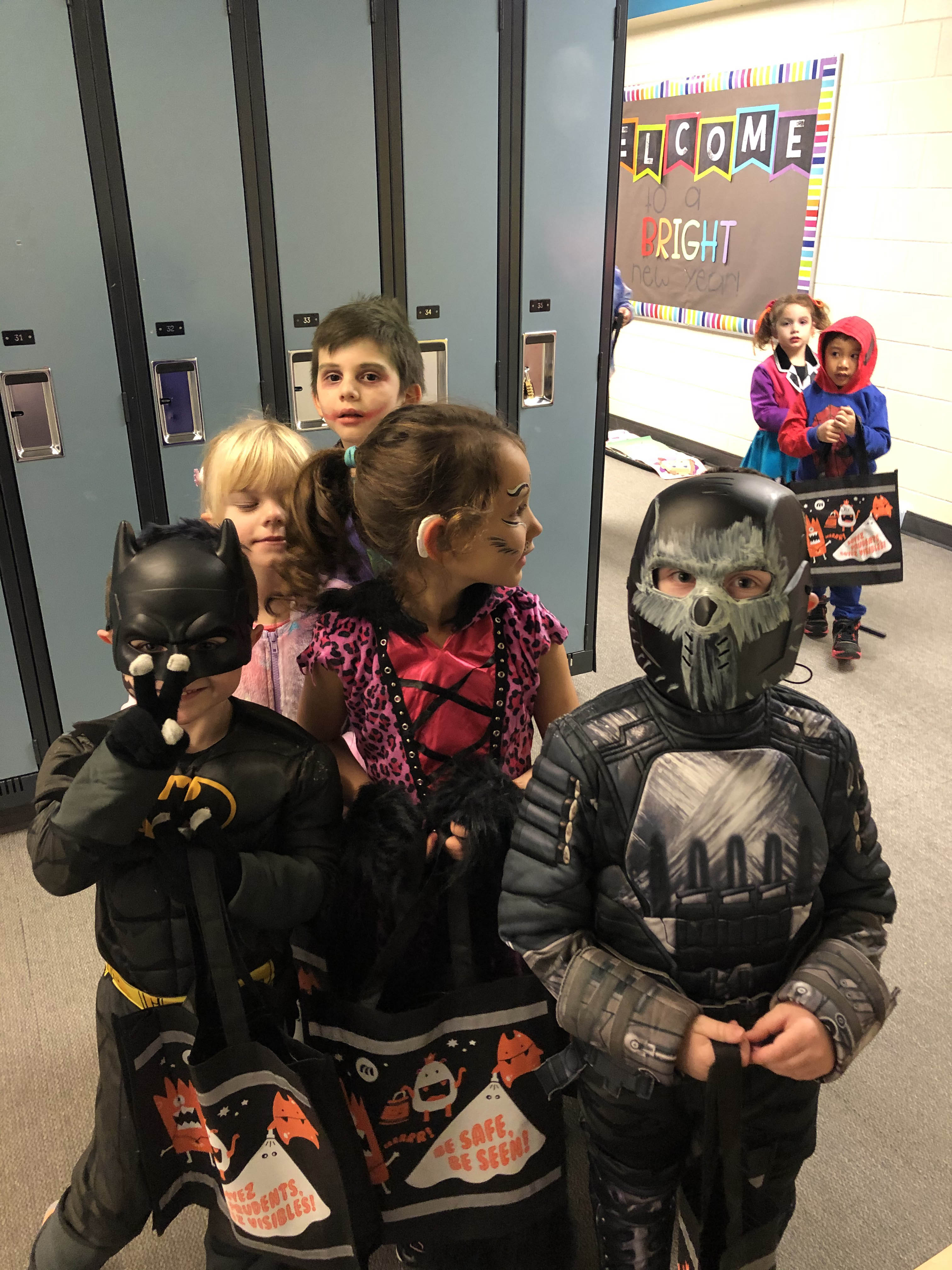 three students in their halloween costumes - batman, jaguar print dress and crossbones
